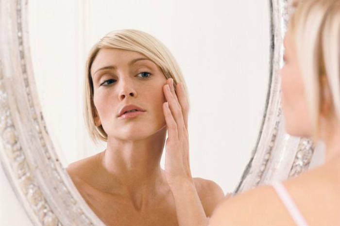 Young-woman-looking-in-mirror-hand-to-face