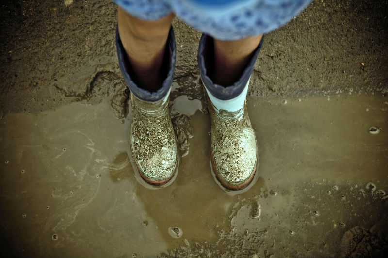 overhead-view-of-childs-legs-wearing-rain-boots-standing-in-mud-puddle