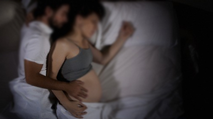 01 Jun 2012 --- Young pregnant woman sleeping with her husband on bed --- Image by © deux/Corbis