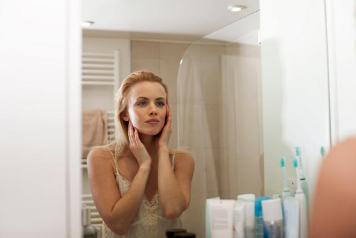 Young woman looking in bathroom mirror