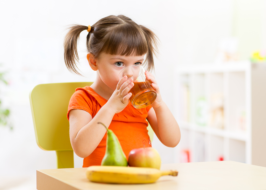 Smiling girl sitting on the table with fruits and juice